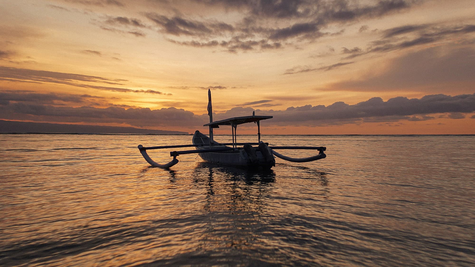 Een traditionele Balinese jukung ligt stil op spiegelglad water onder een brede avondlucht