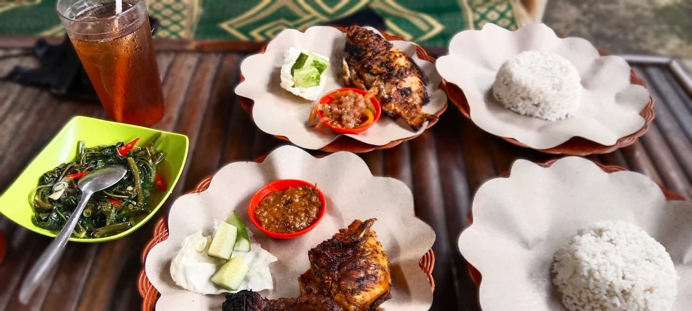 Gegrilde vis met rijst, sambal en komkommer op borden van bananenblad