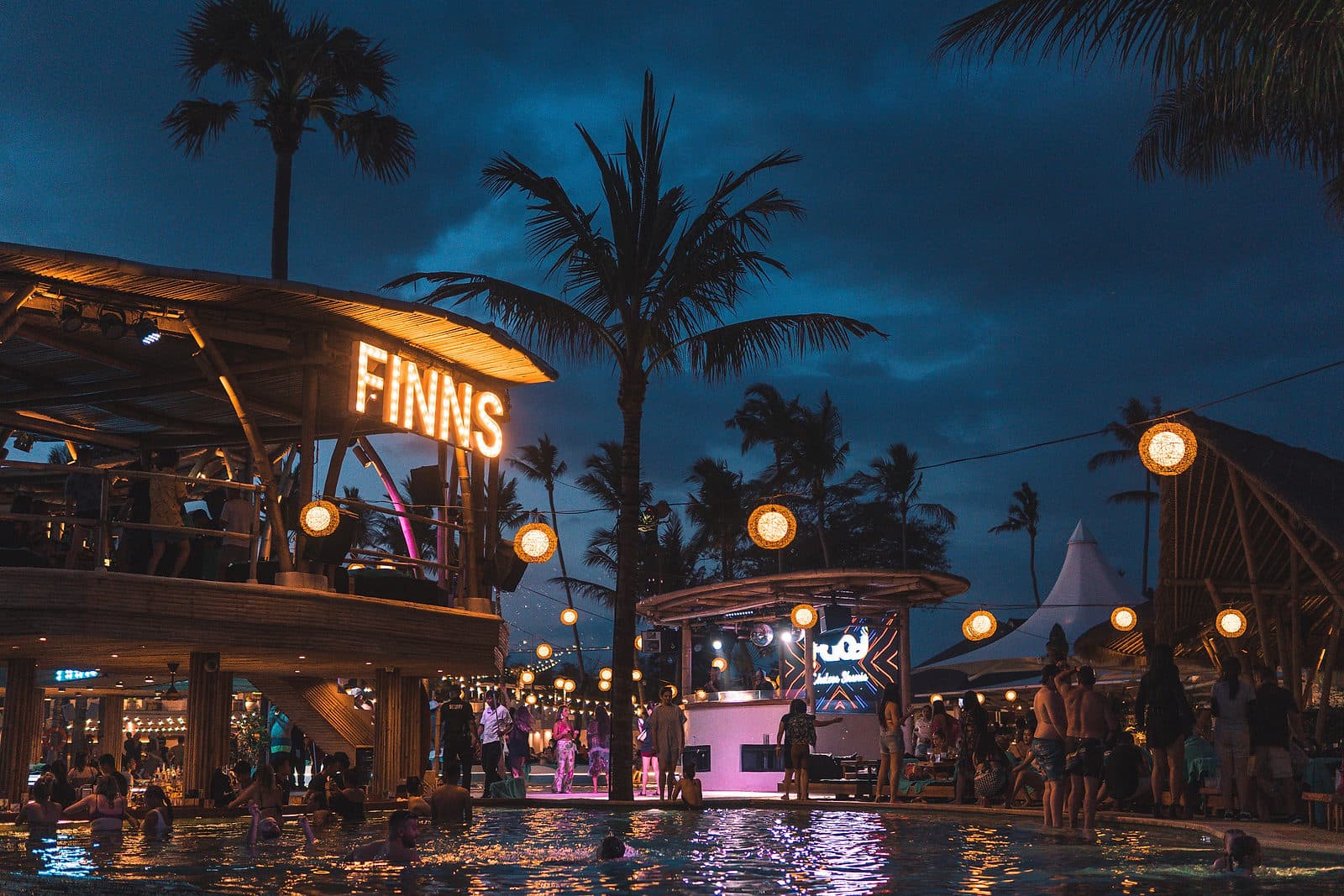 Een beachclub in Canggu bij avond, met verlichte letters en palmen tegen een donkerblauwe lucht