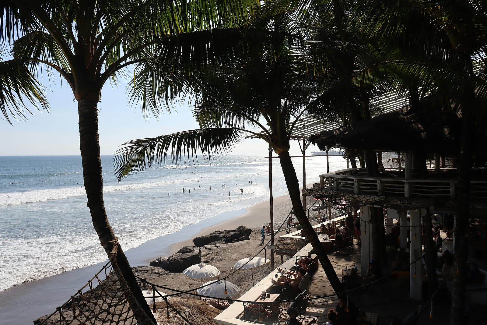 Palmen en strandtenten aan het zwarte zandstrand van Batu Bolong in Canggu op Bali