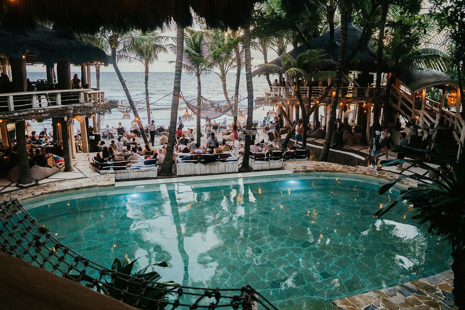 Zwembad met ligbedden en hoge palmen bij een beachclub aan het strand van Canggu