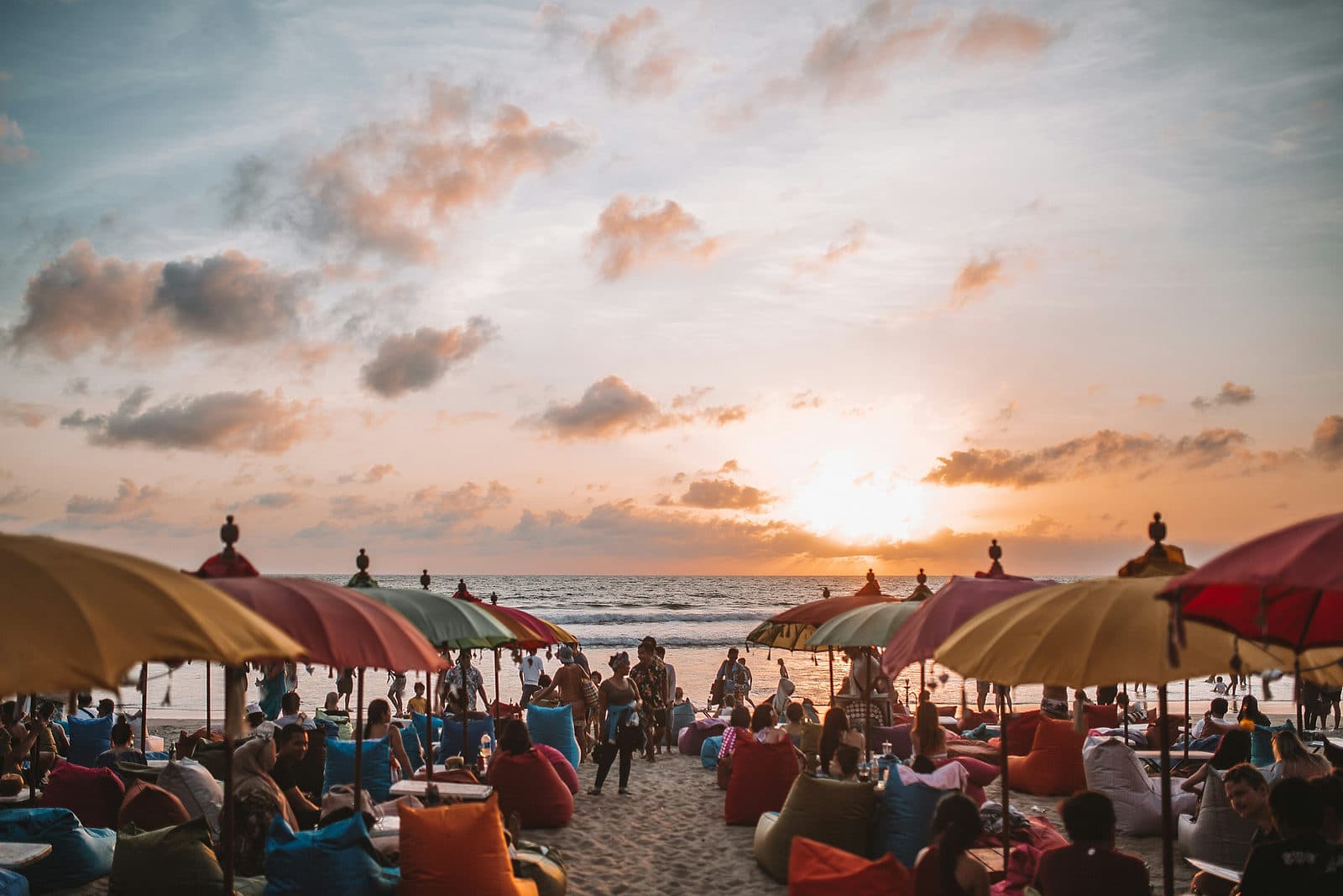 Rijen gekleurde parasols en bezoekers op het strand van Canggu terwijl de zon in zee zakt