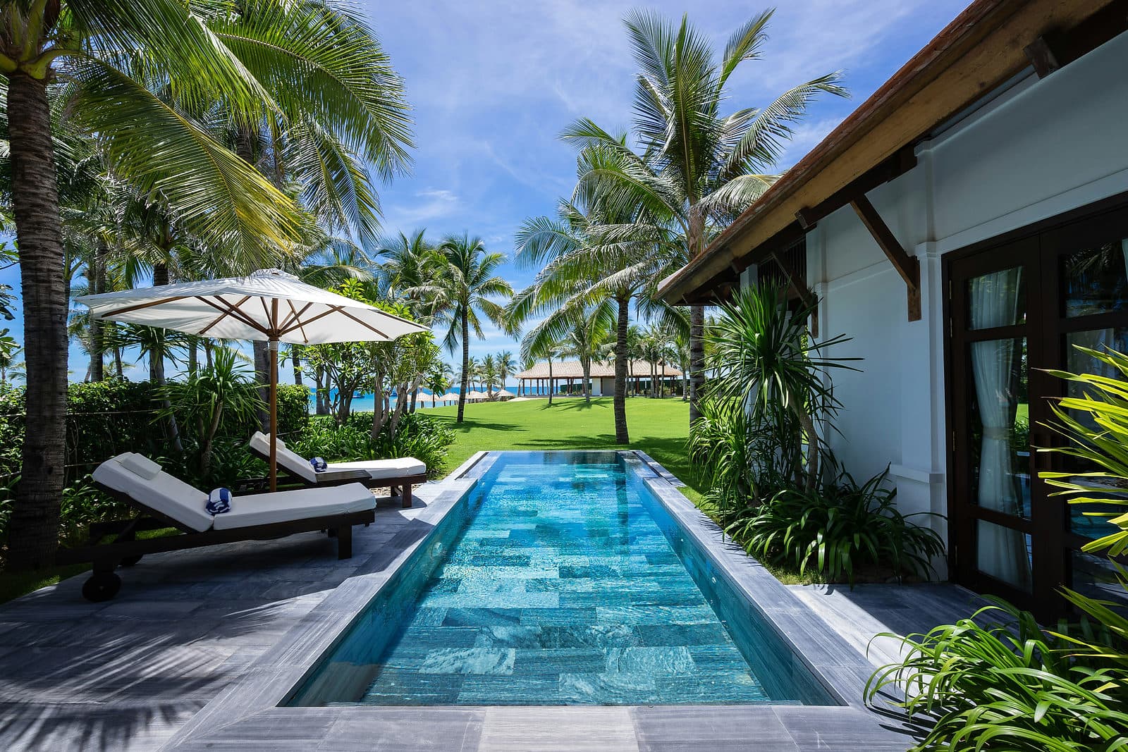 Lang zwembad met ligbedden en palmen met uitzicht op zee bij een resort op Bali