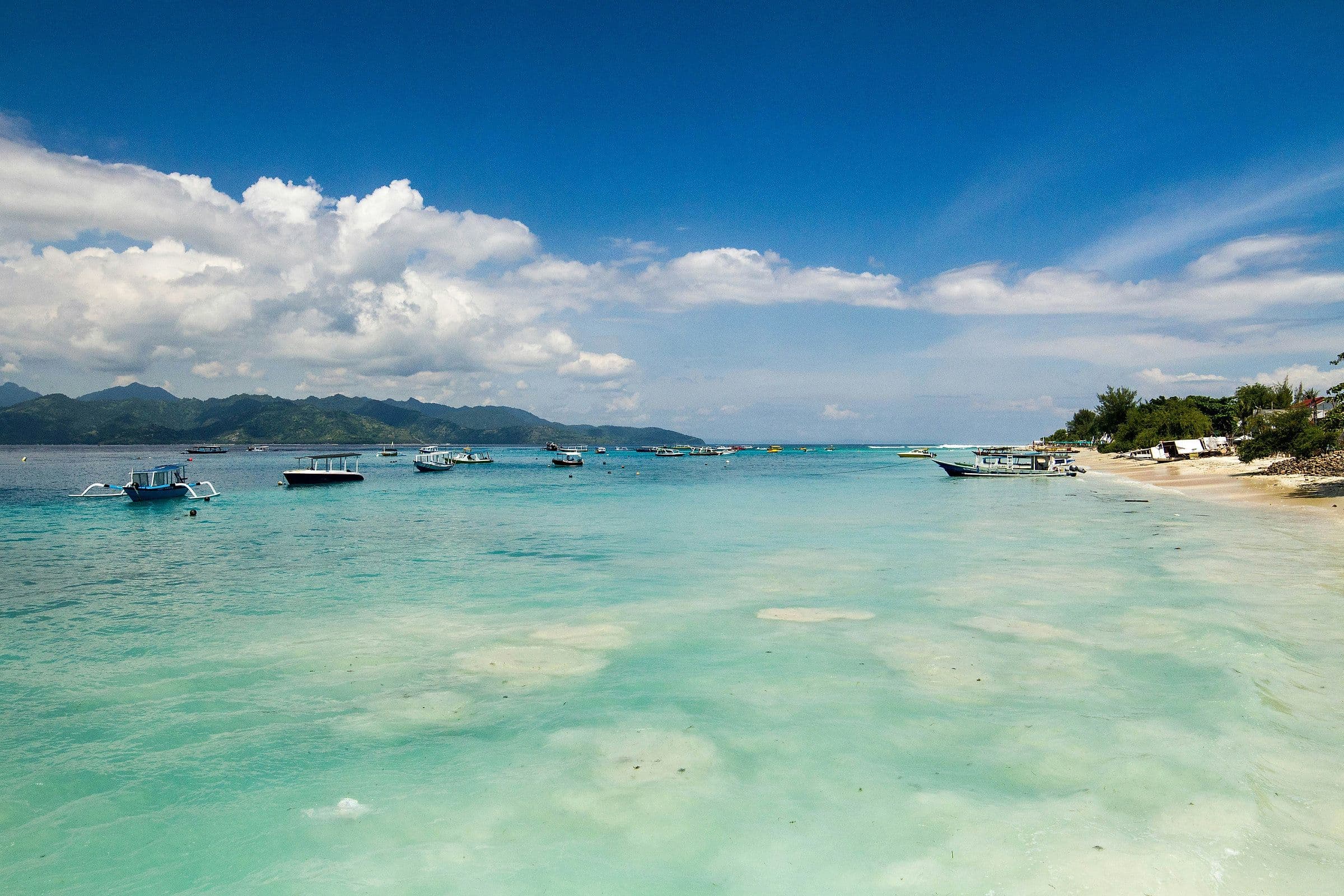 Een baai bij de Gili-eilanden met houten bootjes in ondiep turkoois water
