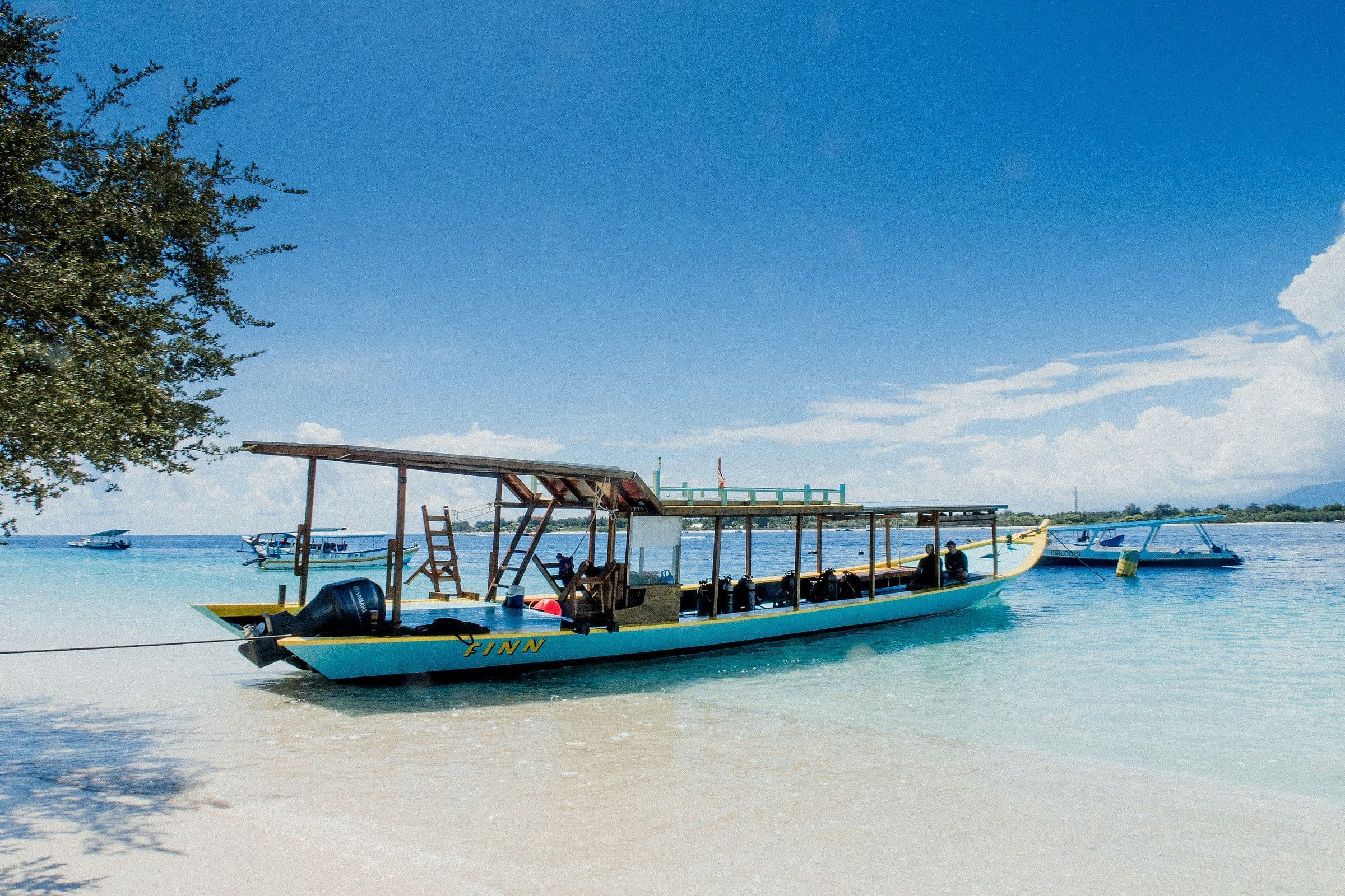 Een traditionele boot ligt in ondiep helder water voor het witte strand van Gili Meno