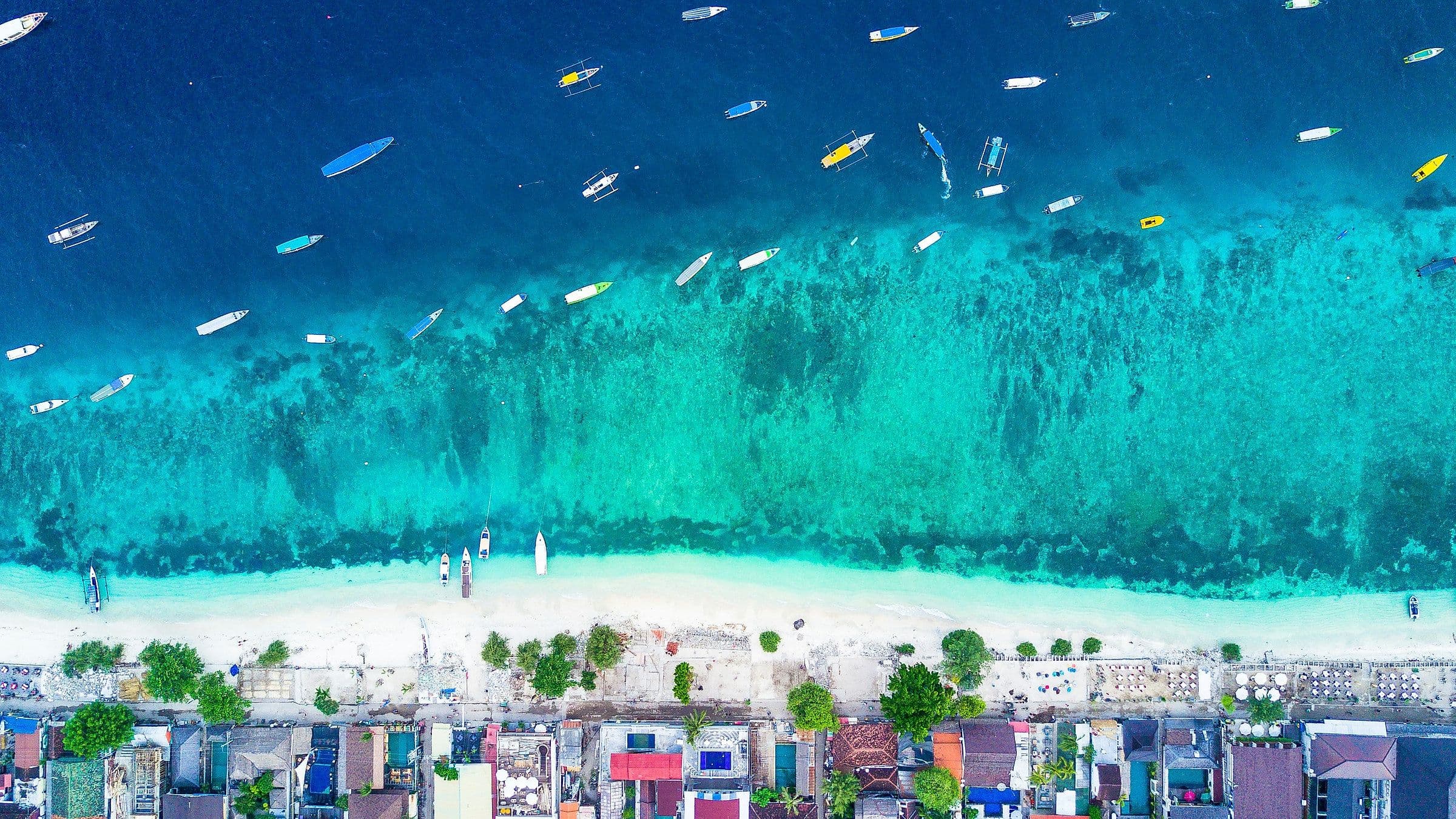 Luchtfoto van de kust van Gili Trawangan, met tientallen bootjes op turkoois water langs een wit strand