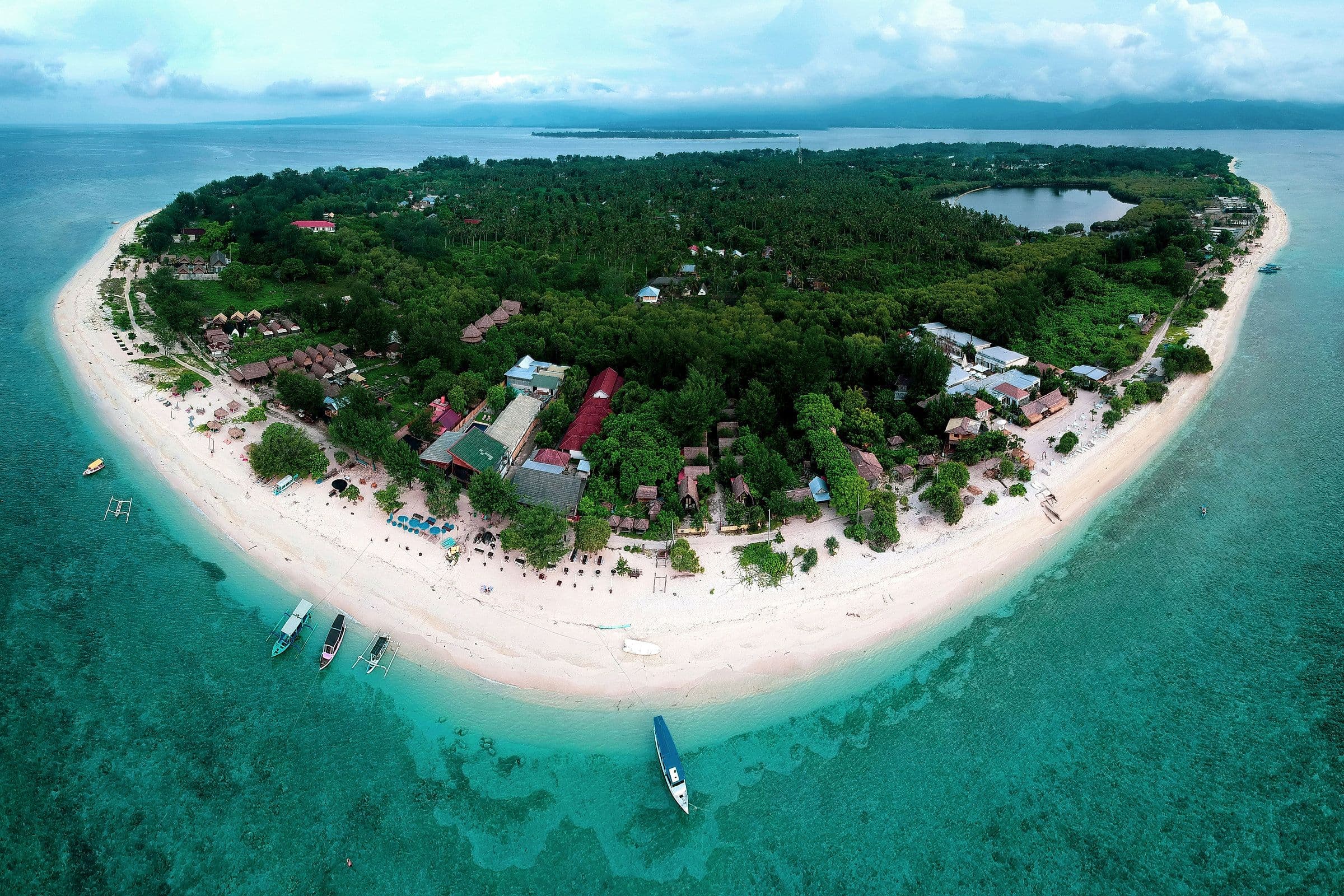 Luchtfoto van een Gili-eiland met een wit strand, bootjes en een groen binnenland