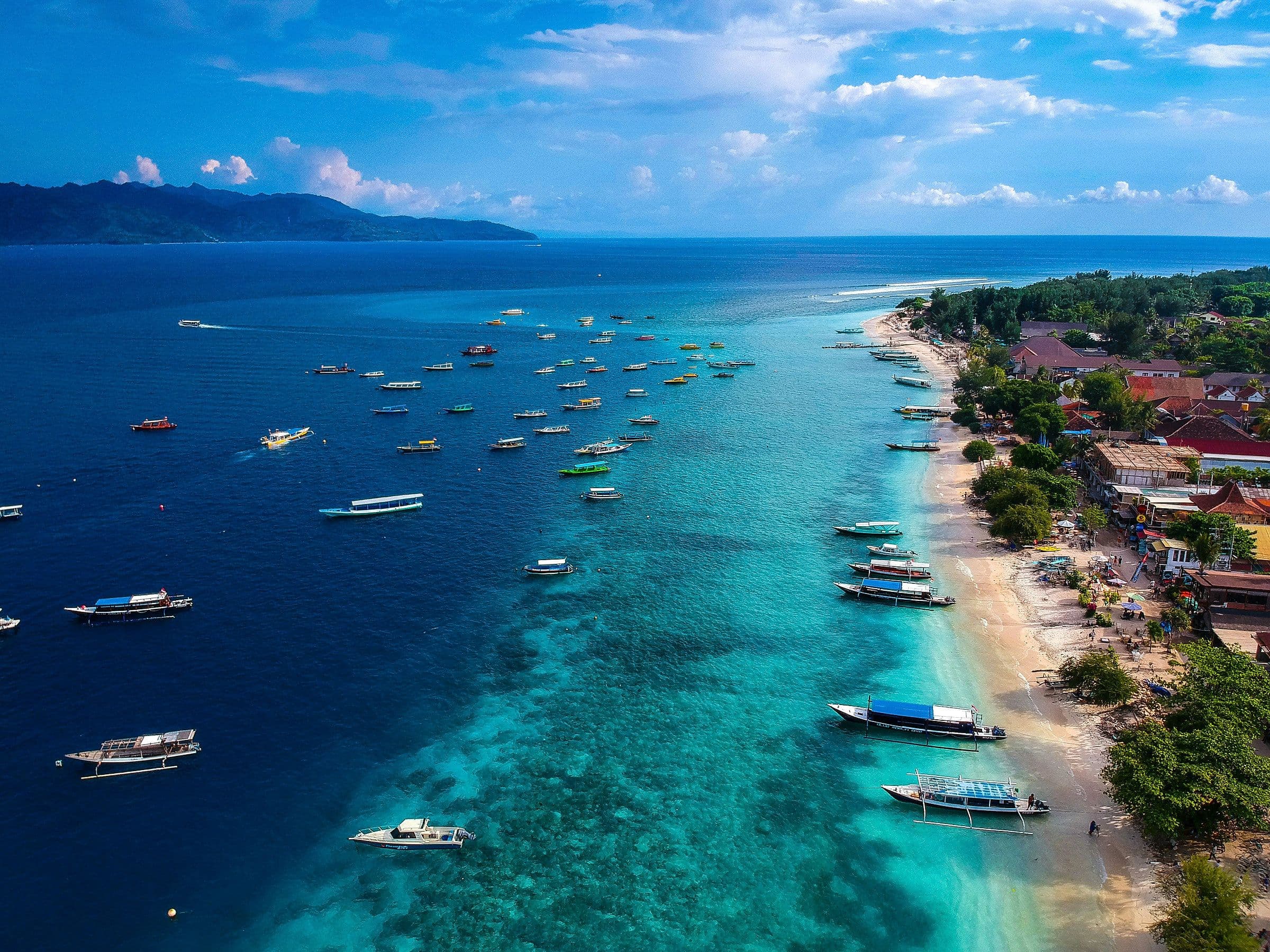 De kustlijn van Gili Air met bootjes voor de kust en de bergen van Lombok op de achtergrond