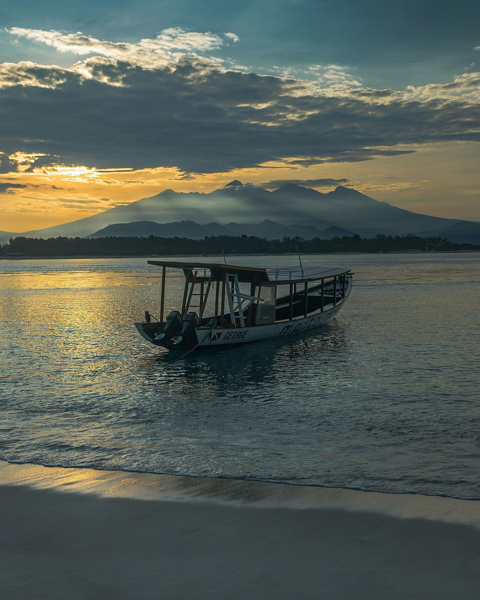 Een houten boot voor de kust van een Gili-eiland met de vulkaan Rinjani op Lombok op de achtergrond