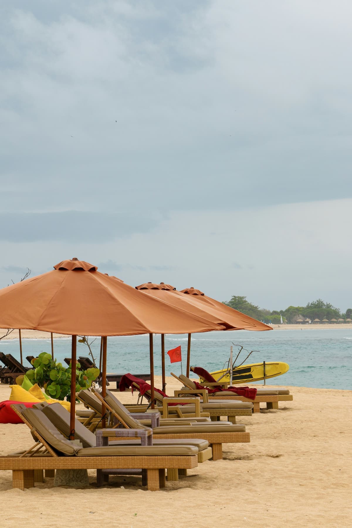 Parasols en ligbedden op het zand van een brede baai met vissersbootjes op Bali