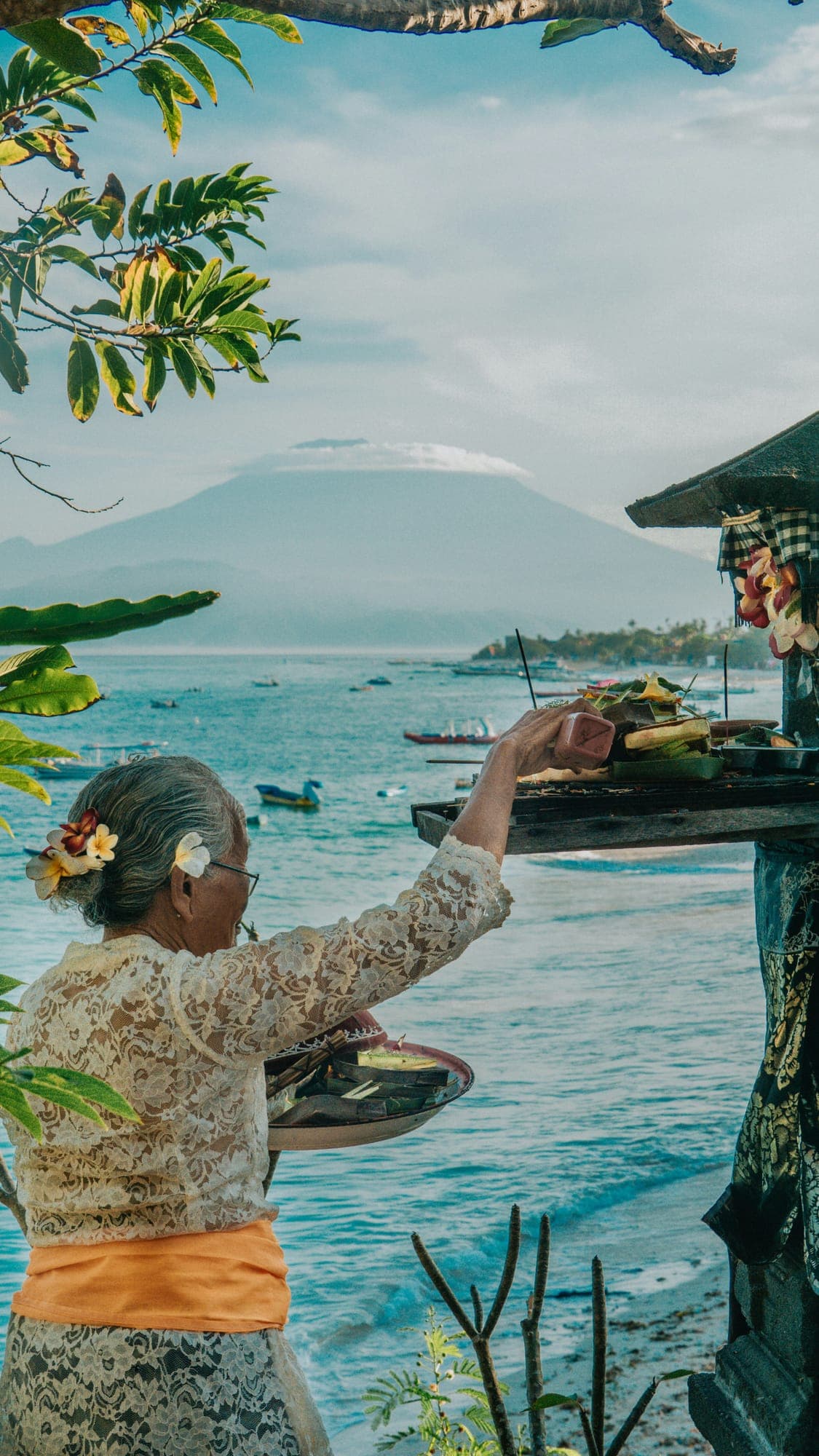 Een Balinese vrouw legt een dagelijks offer neer met de zee op de achtergrond