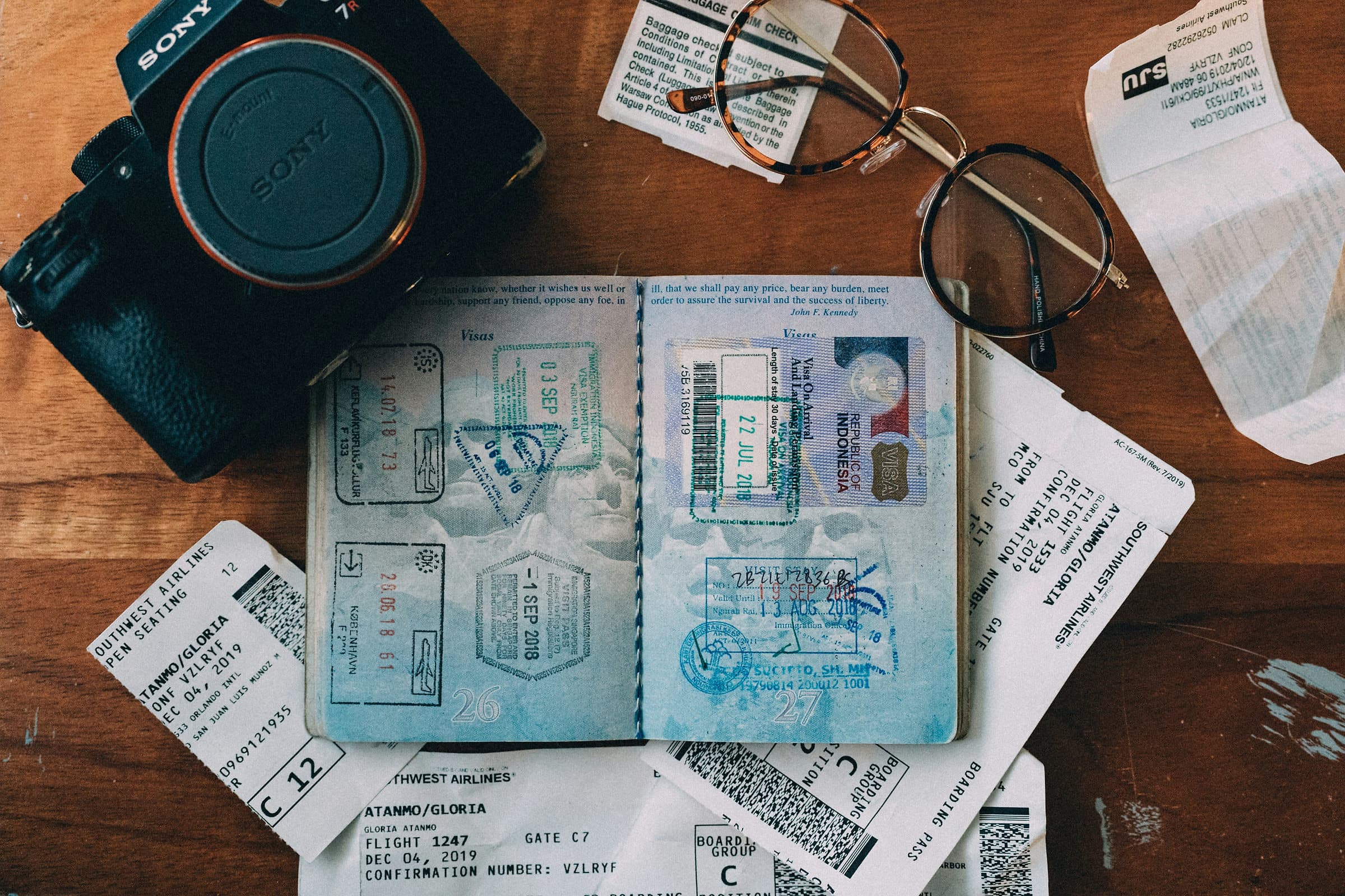 Een opengeslagen paspoort vol inreisstempels met een Indonesisch visum, boardingpasses en een camera op een houten tafel
