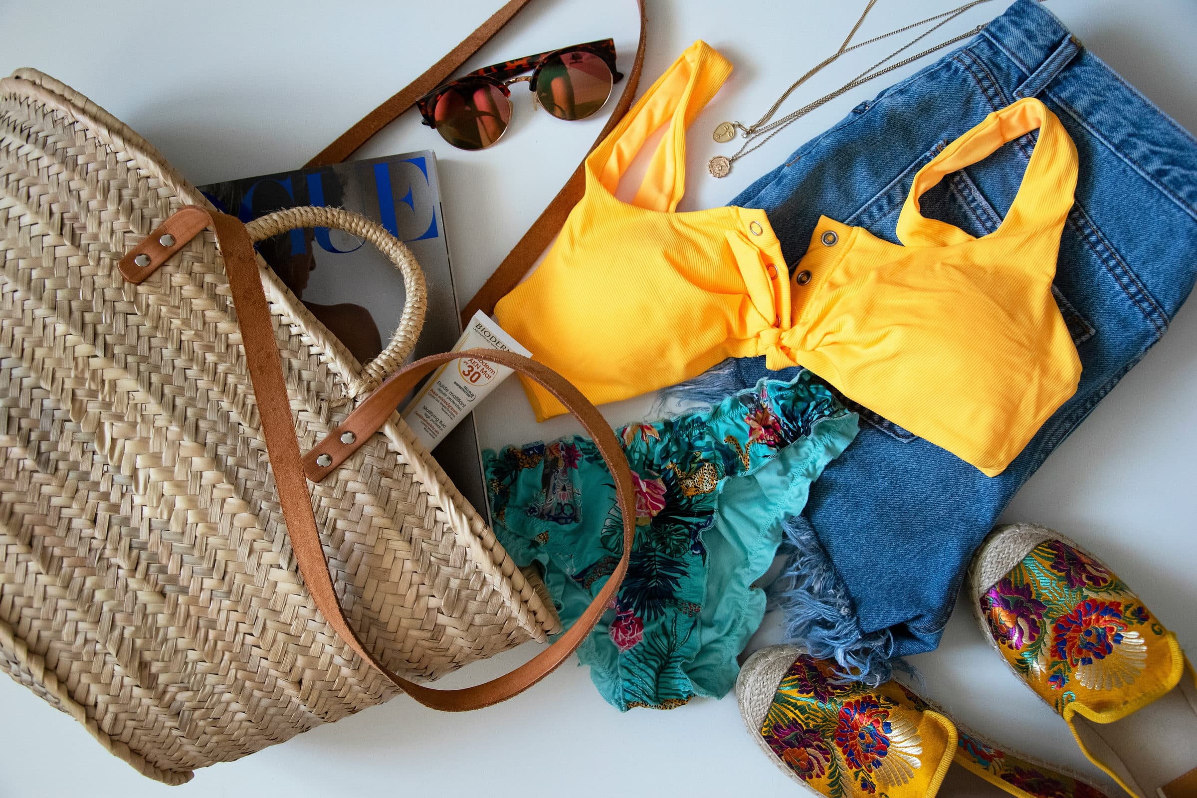 Een strandtas met bikini, zonnebrand en zomerkleding klaar om in te pakken