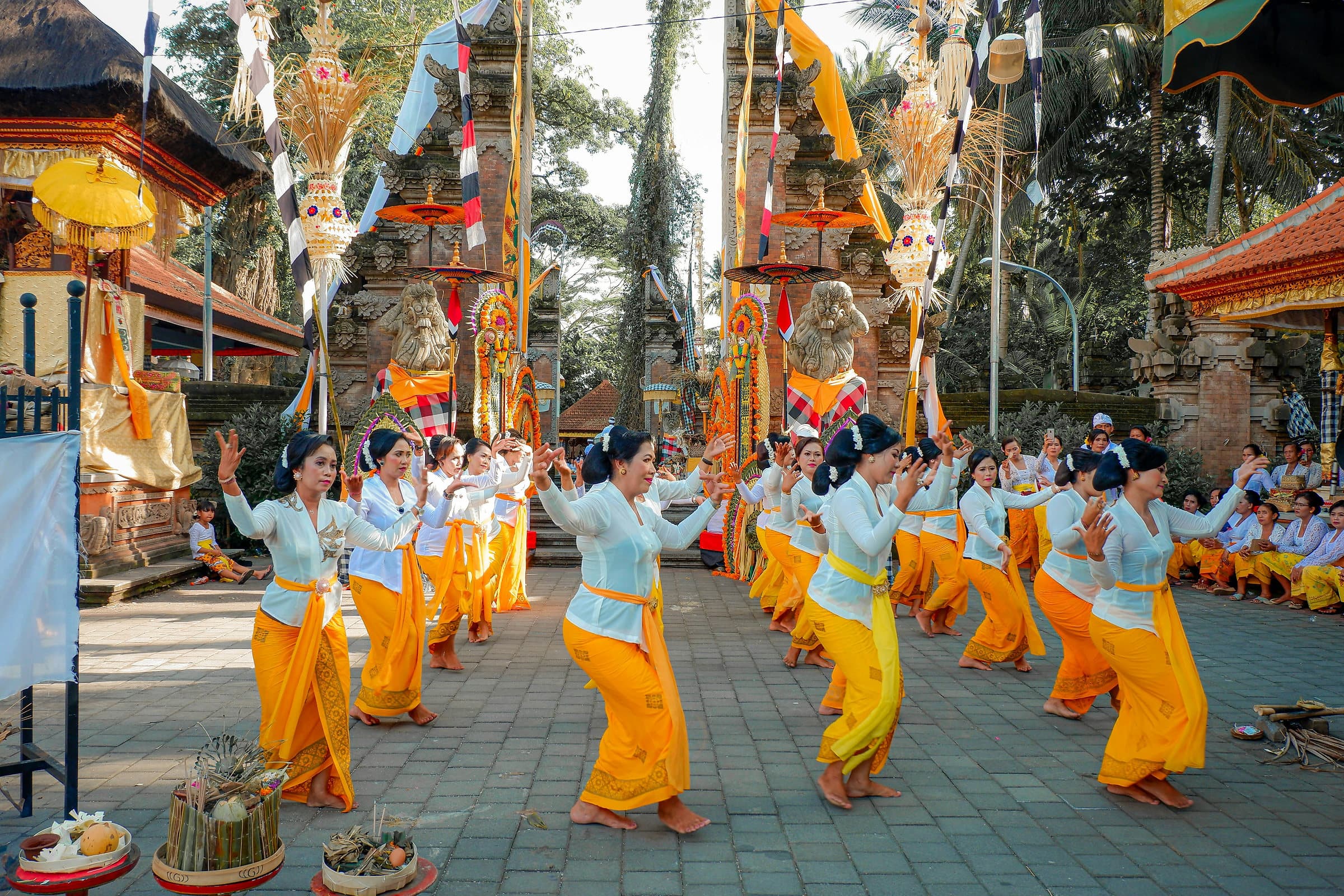 Balinese danseressen in witte kebaya en oranje sarong tijdens een ceremonie op een tempelplein
