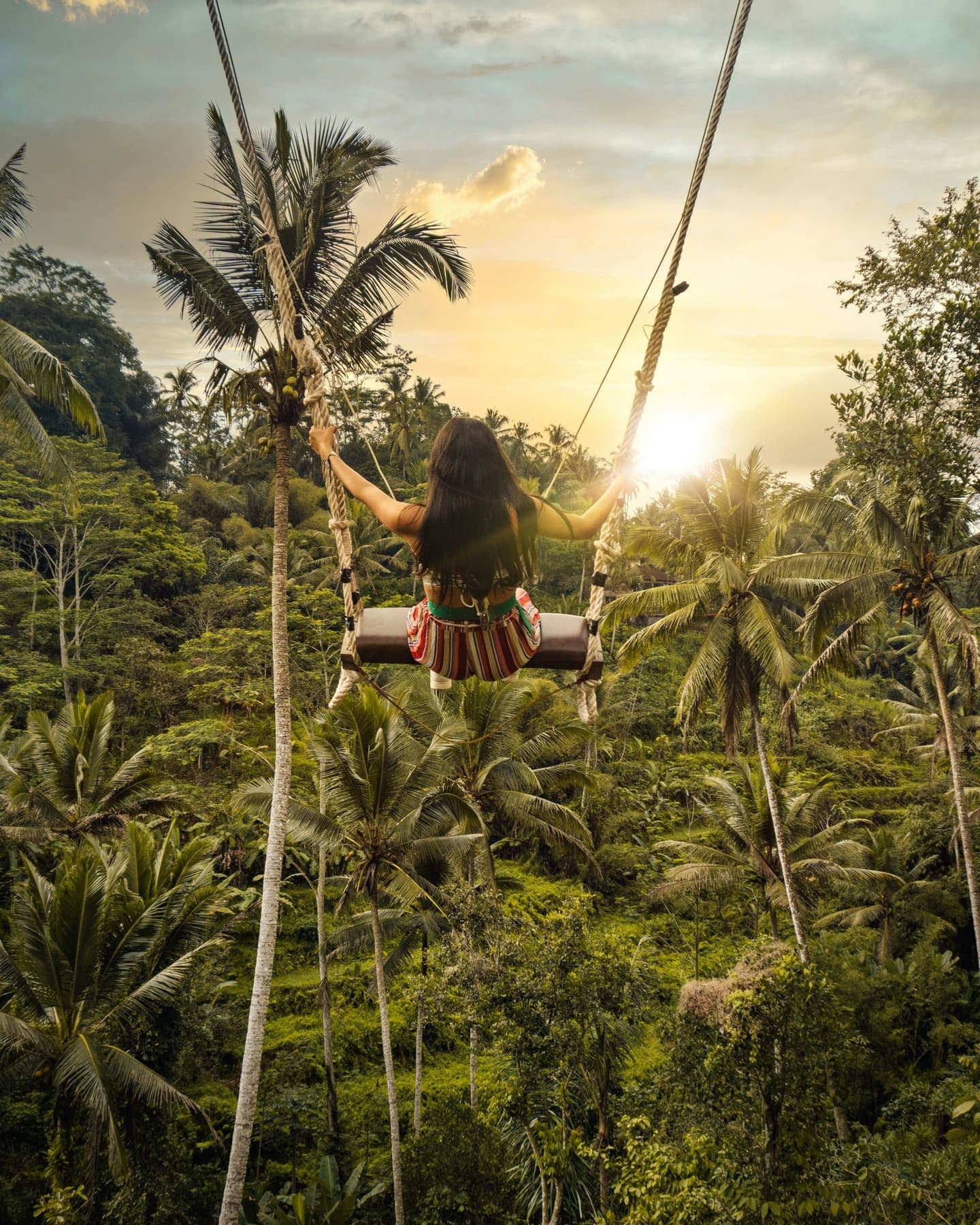 Iemand schommelt hoog boven een groene jungle-vallei bij Ubud in het late licht
