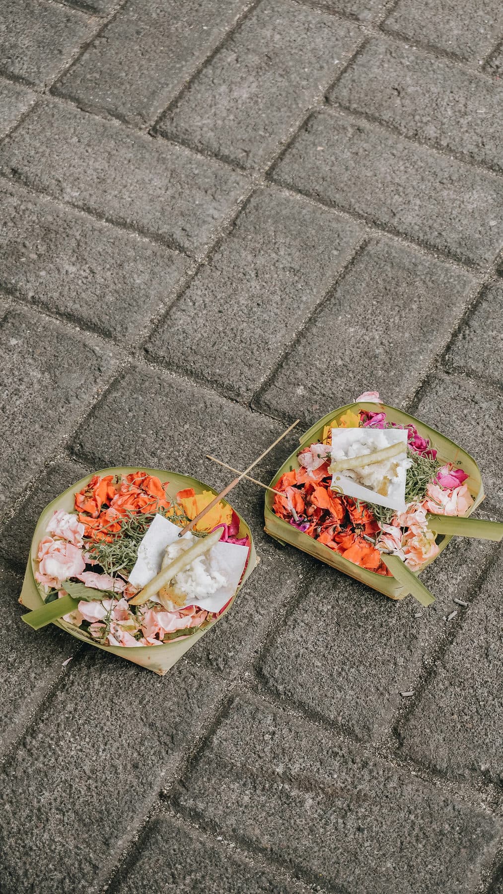 Twee canang sari, kleine offerbakjes met bloemen, op de stoep van een Balinese straat