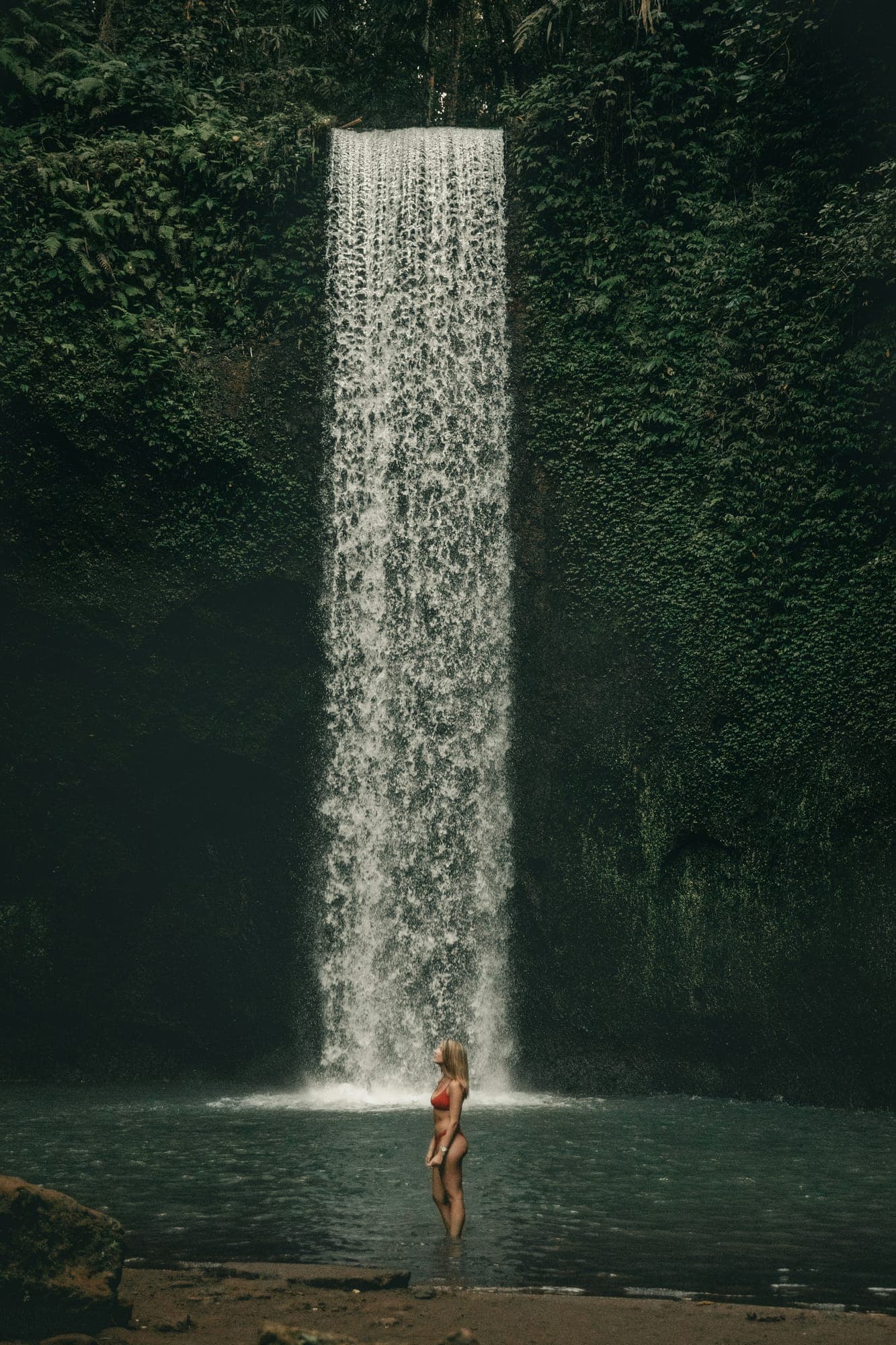 Een smalle waterval stort tussen groene, begroeide rotswanden naar beneden in de jungle