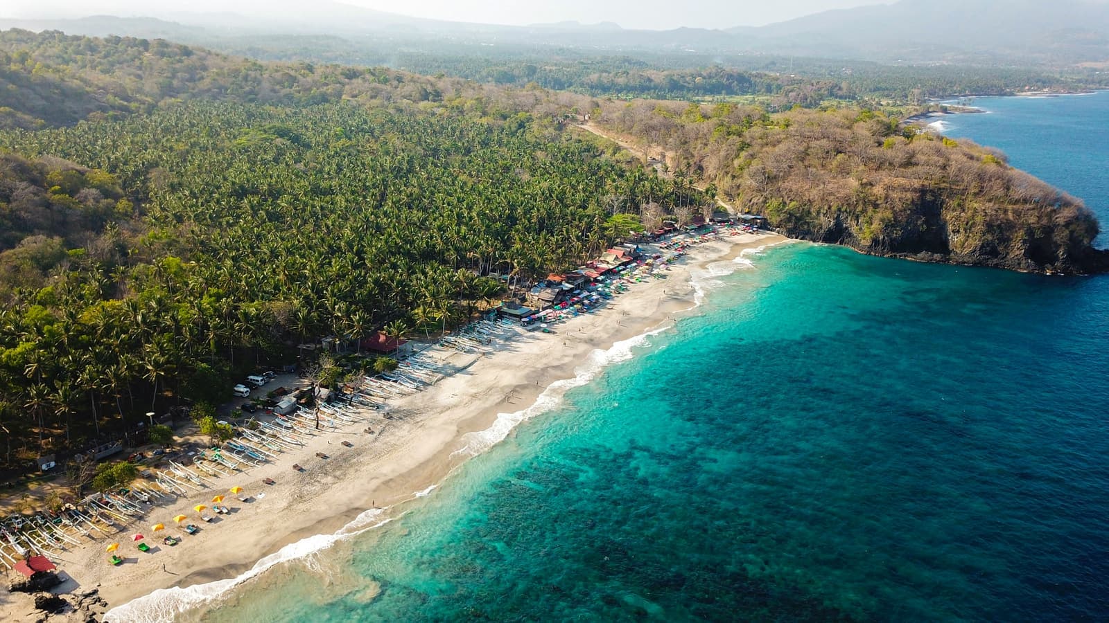 Baai met wit zand, warungs langs het strand en turkoois water gezien vanaf de klif op Bali