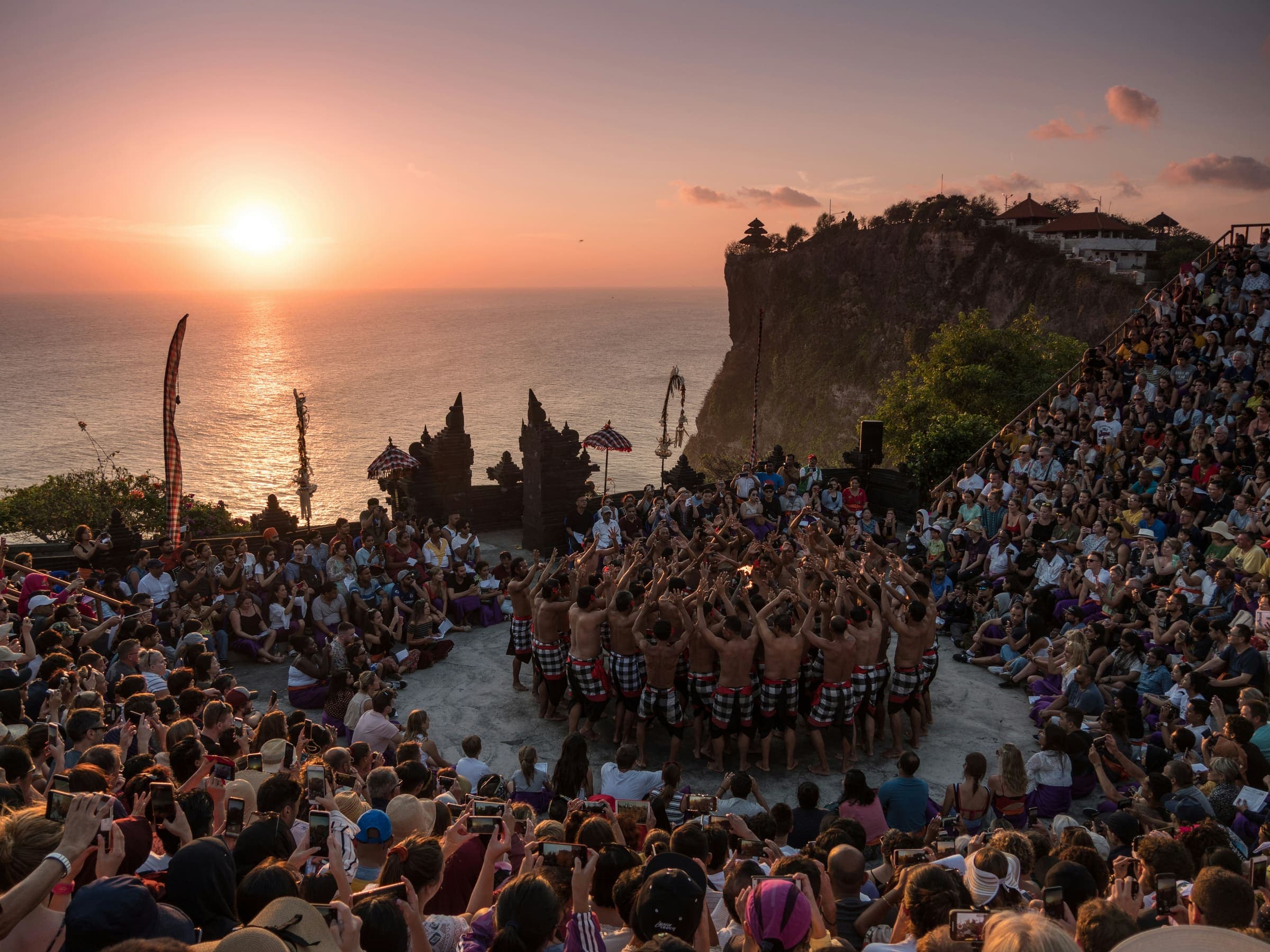 Publiek kijkt naar de Kecak-vuurdans in het openluchttheater op de kliffen van Uluwatu bij zonsondergang