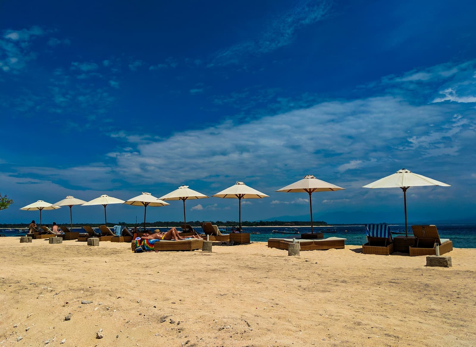 Rieten parasols en ligbedden op een breed wit strand aan een blauwe zee op Bali