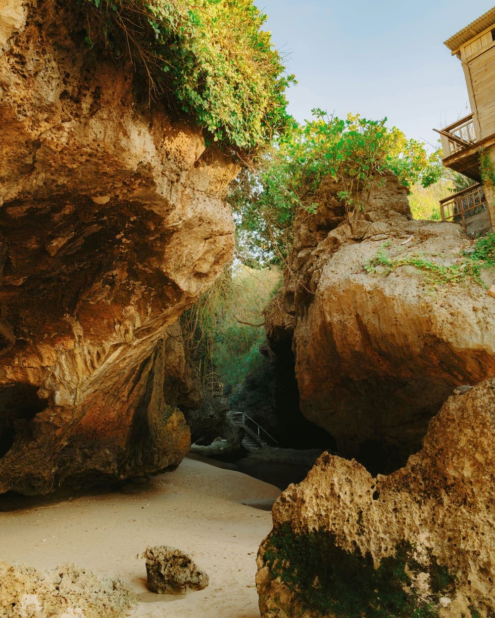 Smalle doorgang tussen hoge rotsblokken met een trap naar het strand bij Uluwatu op Bali
