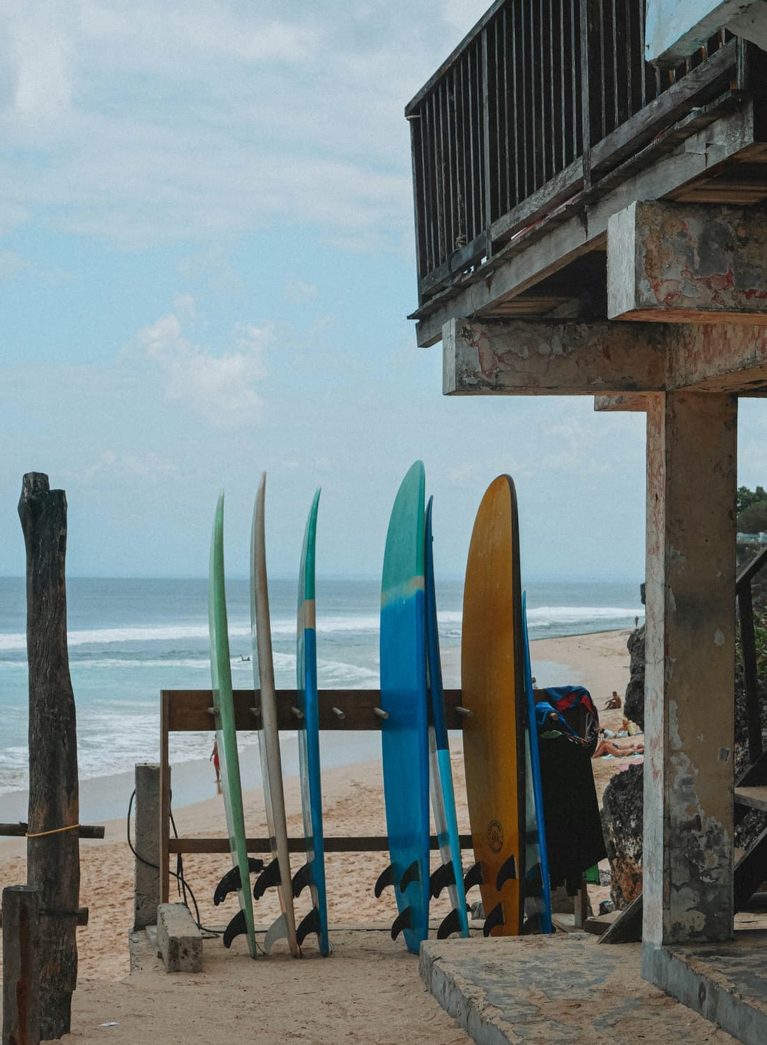 Surfplanken staan naast elkaar tegen een houten rek met de zee op de achtergrond