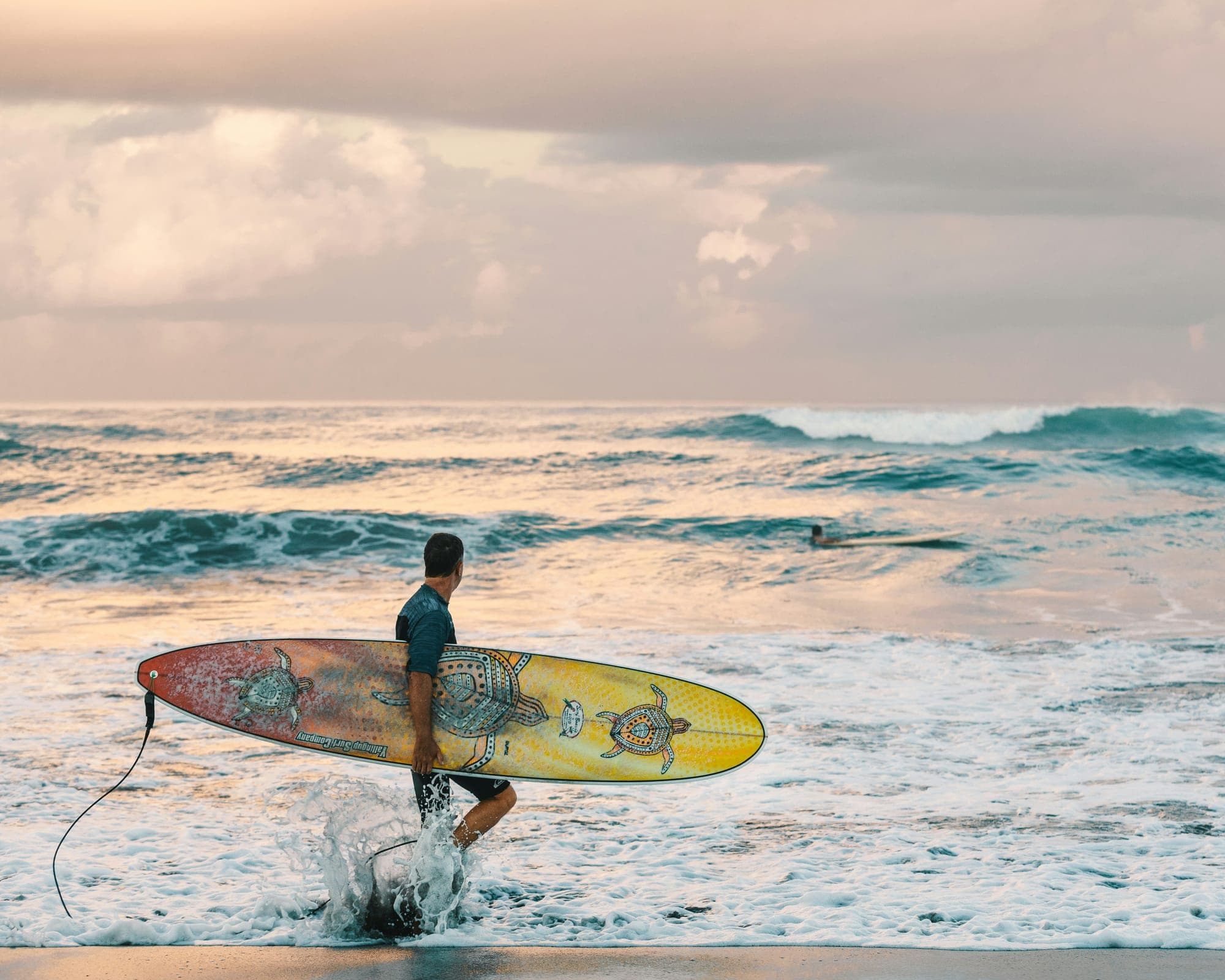 Een surfer loopt met zijn board het schuimende water in