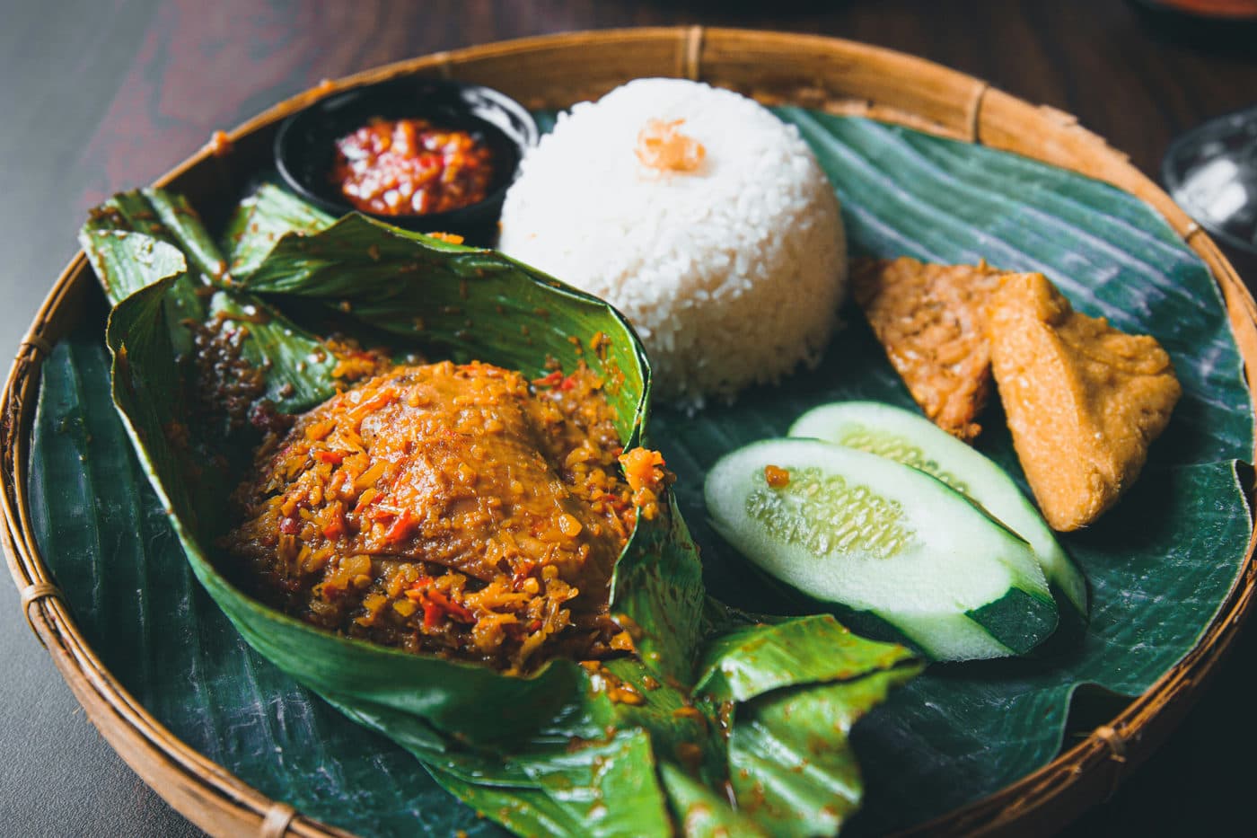 Nasi campur op een bananenblad in een gevlochten mandje, met rijst, sambal en groente