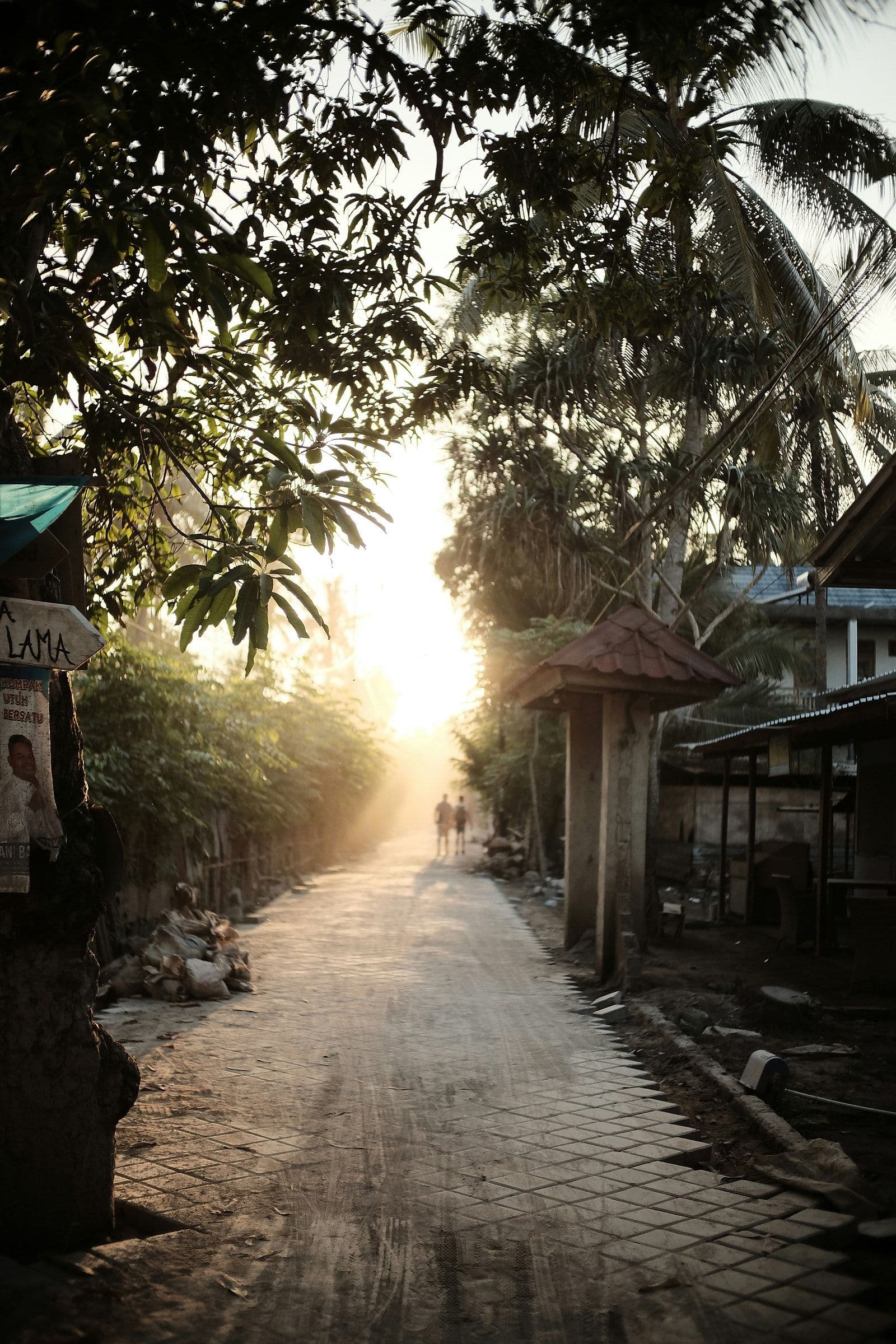Een zandpad tussen de huizen en palmen op een Gili-eiland in het late middaglicht