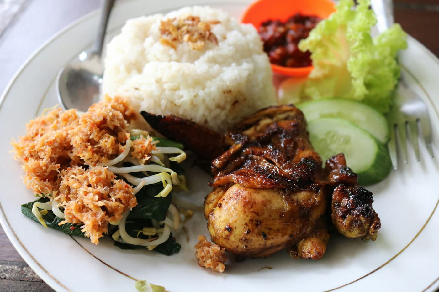 Een bord met rijst, gebakken kip, groente en sambal zoals dat bij een homestay wordt opgediend