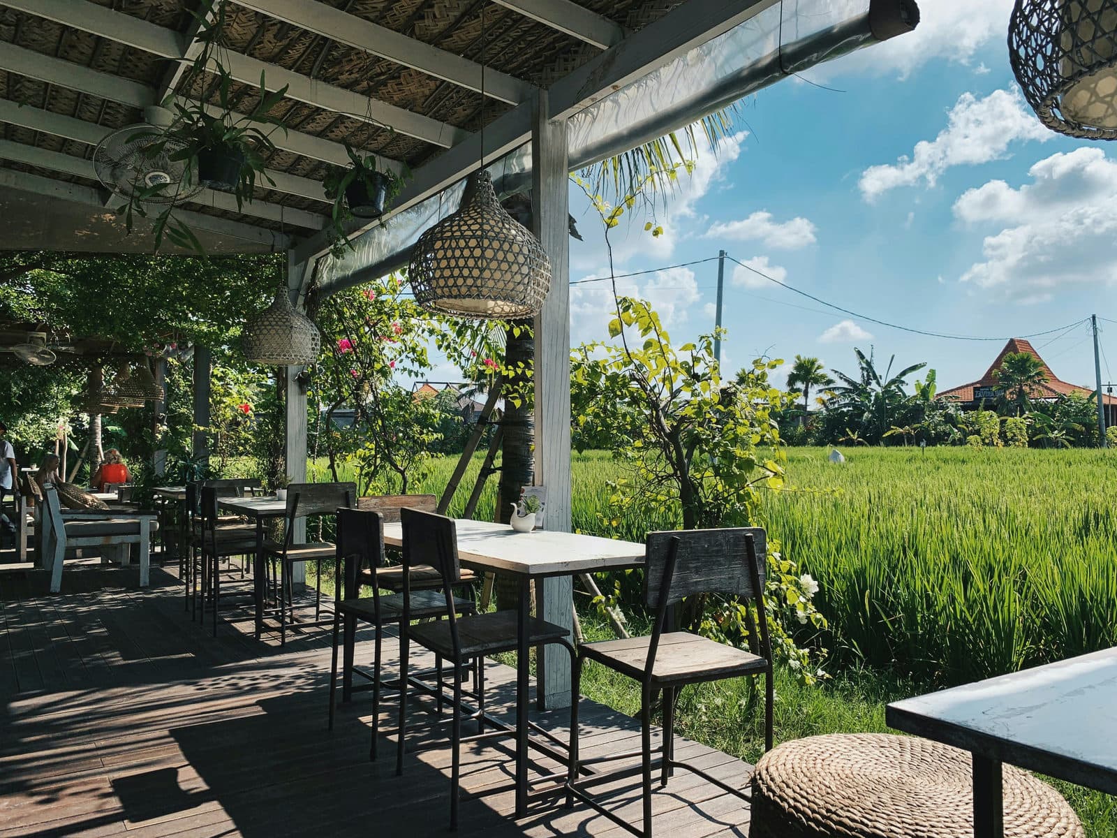 Een open restaurantterras met tafels en uitzicht over groene rijstvelden en palmen
