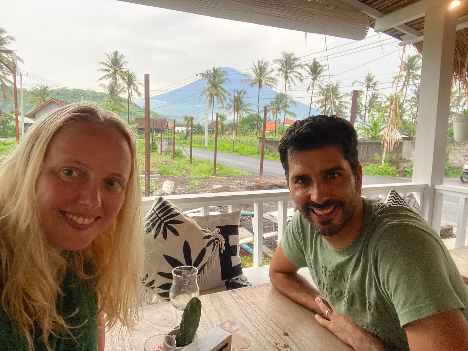 Twee reizigers op een terras met uitzicht op palmen, rijstvelden en de vulkaan Agung