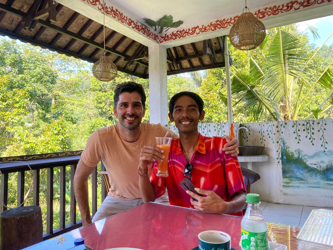 Twee mannen proosten met een glas sap op het overdekte terras van een warung in de jungle