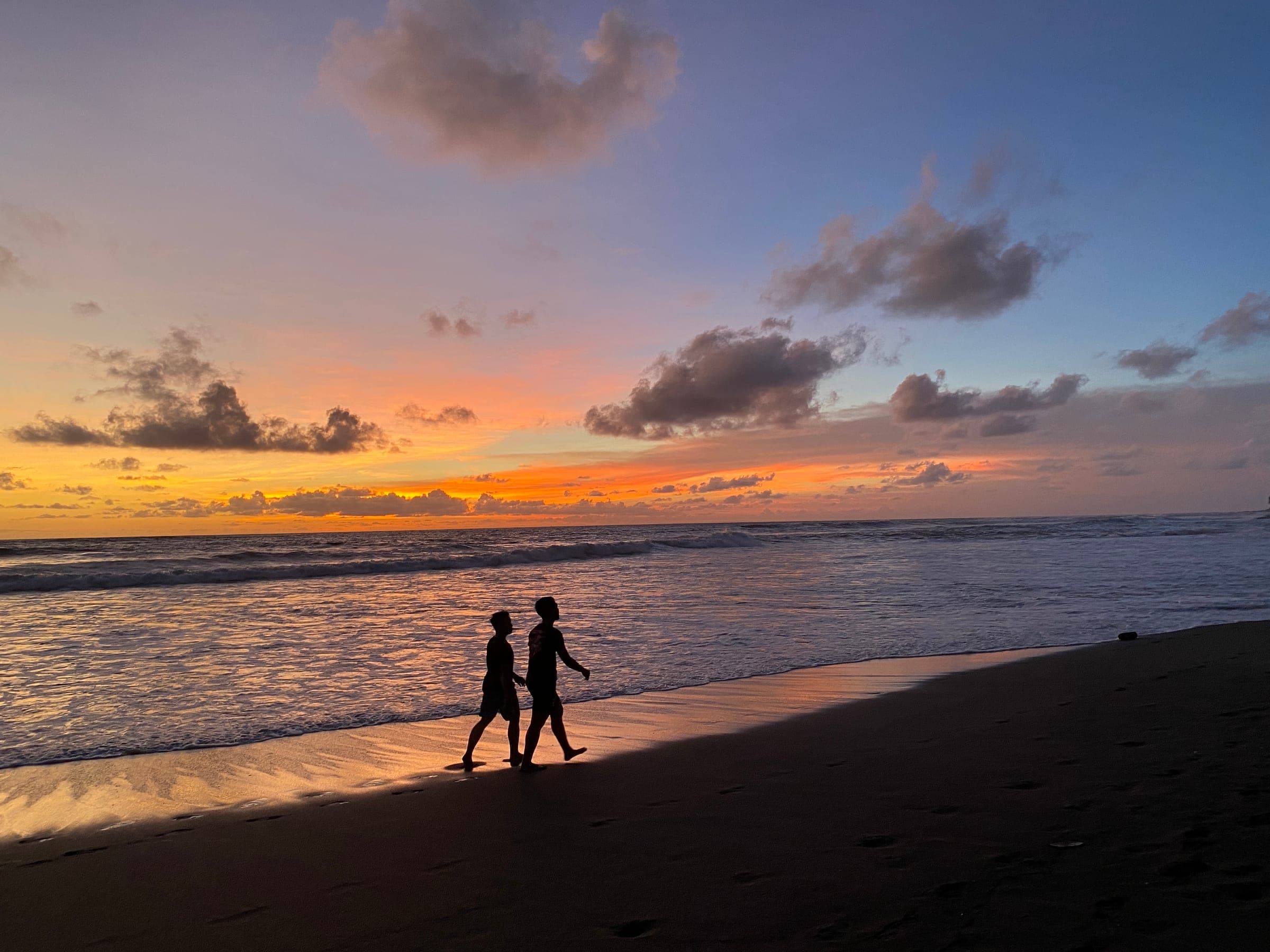 Twee wandelaars als silhouet op het strand van Bali bij zonsondergang