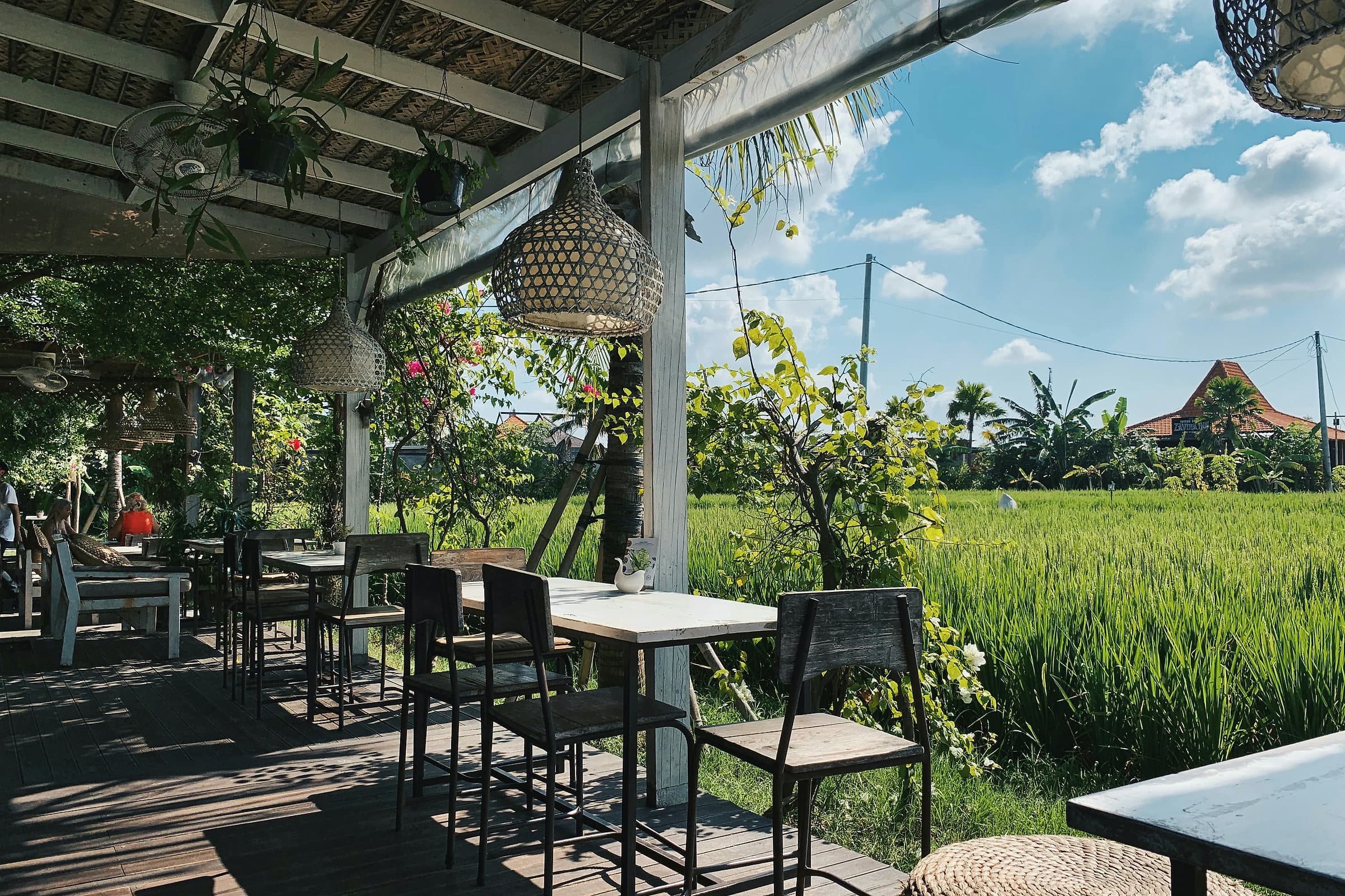 Open restaurantterras op Bali met houten tafels en rieten lampen, uitkijkend over een groen rijstveld